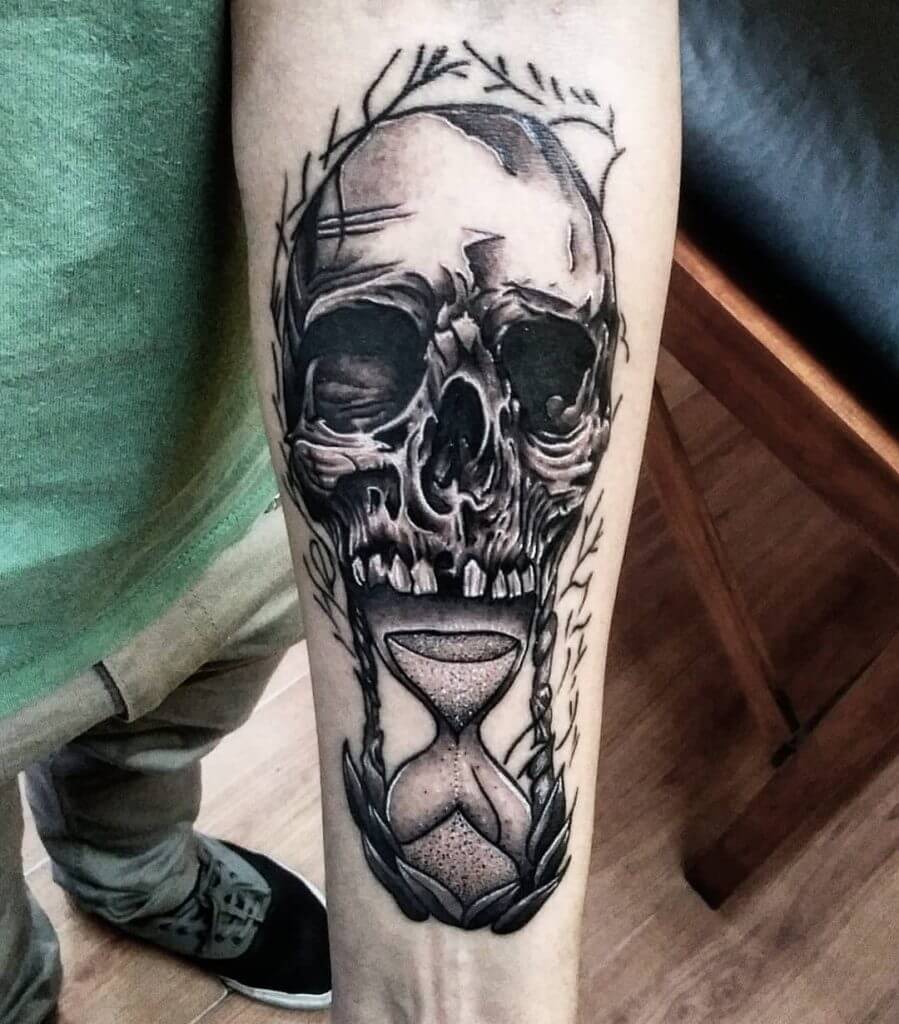 Black Male tattoo of a skull with an hourglass on the left forearm