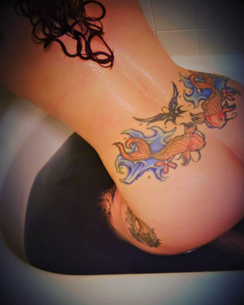 Color womans tattoo of a Koi fish on the lower back