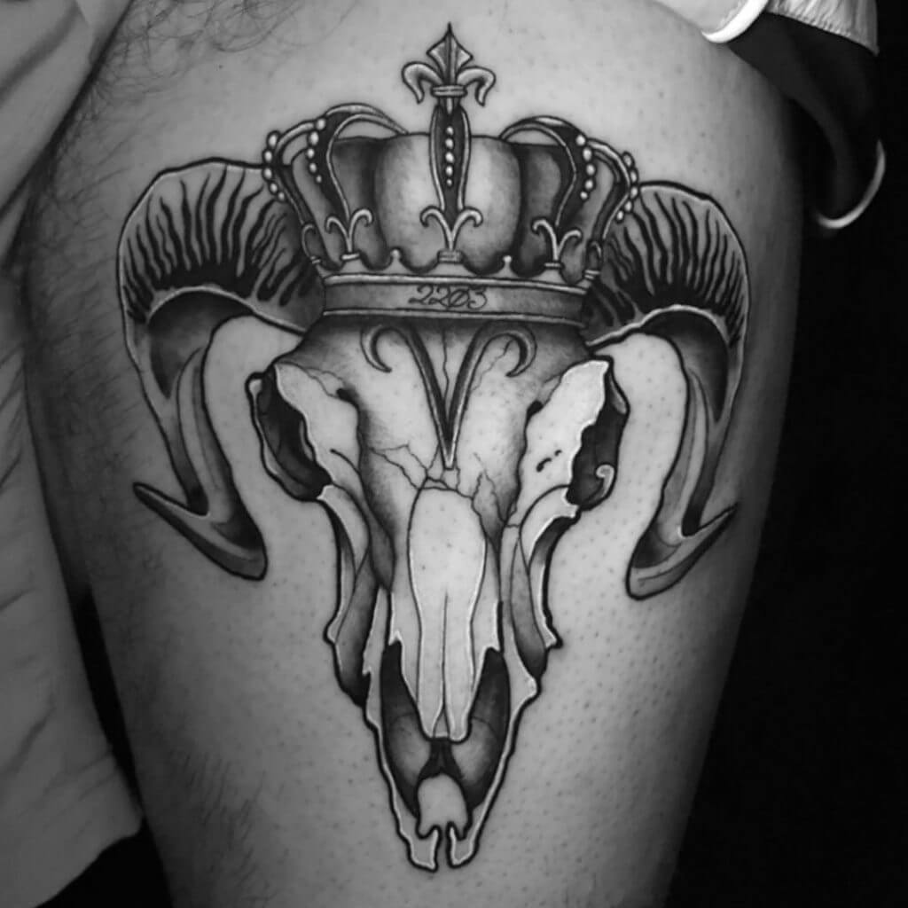Mens black neo traditional tattoo of a ram skull with a crown on the left thigh