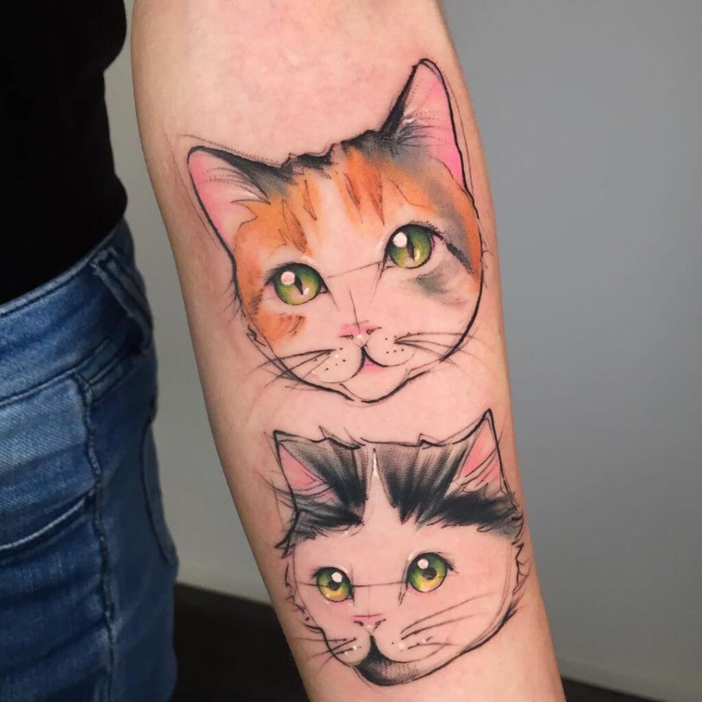 Women color cartoon tattoo of a two cats head on the left forearm