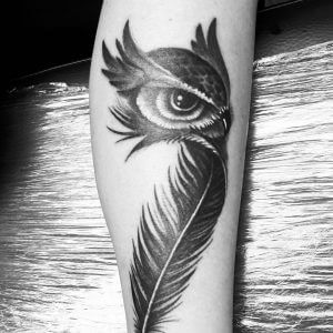 Black owl tattoo with a feather for women on the left calf
