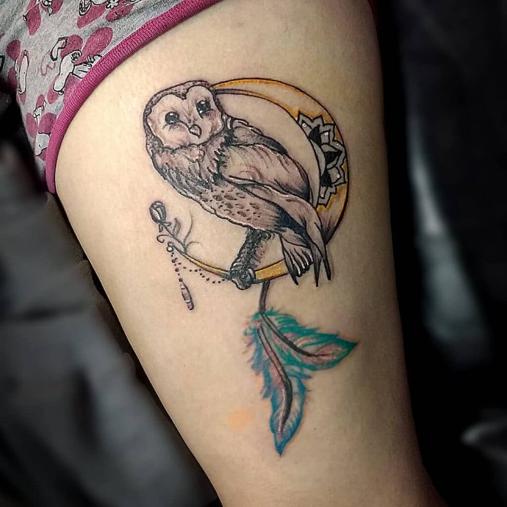 Black owl tattoo with a moon and feathers for women on the left thigh