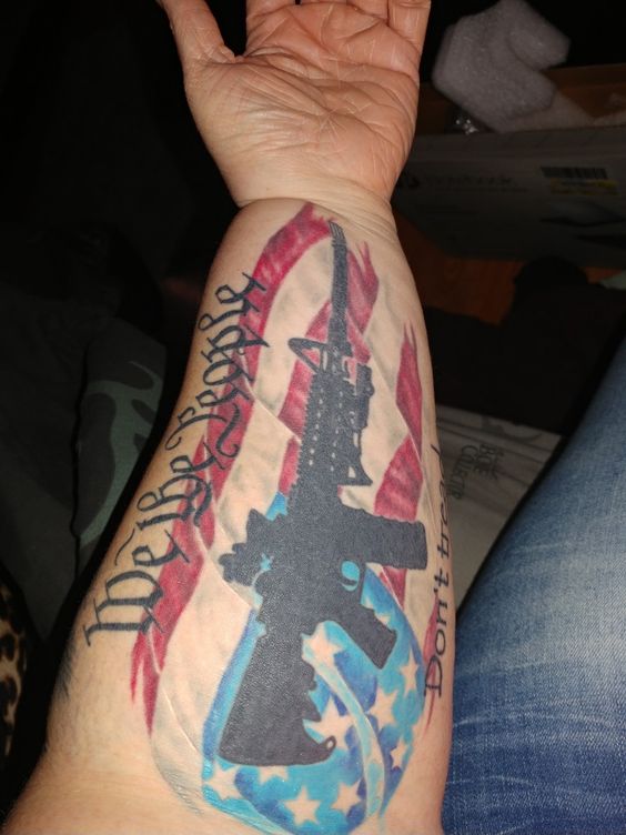 Forearm We the People tattoo with a flag and gun